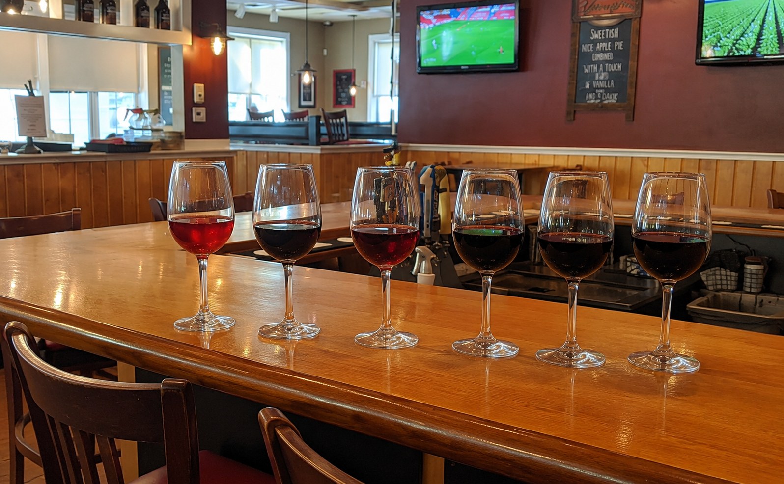 Six glasses of red wine lined up on the bar at Adam's Grille Kent Island for Half-Price Wine Wednesday